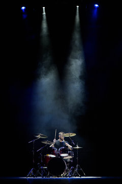 music, people, musical instruments and entertainment concept - male musician with drumsticks playing drums on the stage.