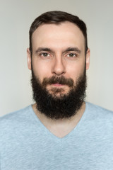Obraz premium Portrait of a beautiful real hipster man with a full face of a beard and mustache on a light background in a barber shop in a gray shirt