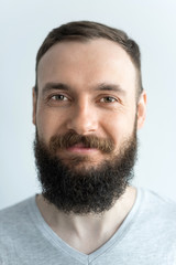 Obraz premium Portrait of a beautiful real hipster man with a full face of a beard and mustache on a light background in a barber shop in a gray shirt