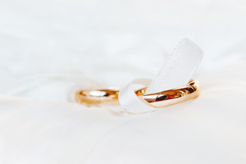 Golden wedding rings on white silk background. Wedding details. Symbol of love and marriage.