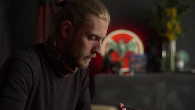 Portrait of concentrated man involved in griding process, and sharpening his knife manually with whetstone indoor in slow motion