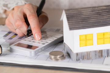 Young woman makes some calculations. Small paper house, coins, car in the background.