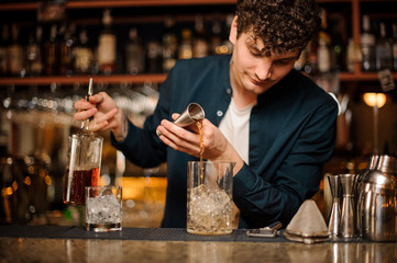 barman prepares an alcoholic cocktail , adding alcohol to the ice