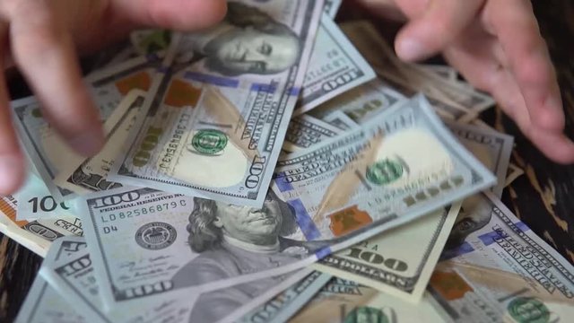 hand rakes dollar bills on a wooden table, background of banknotes
