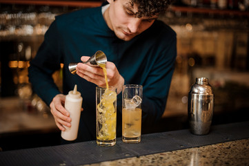 young barman prepares two alcoholic cocktails