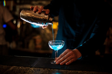 barman pours from a shaker into a glass of alcohol cocktail Blue Lagoon