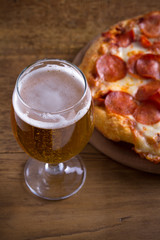 Beer and pepperoni pizza on wooden table. Glass of beer. Ale and food concept. vertical
