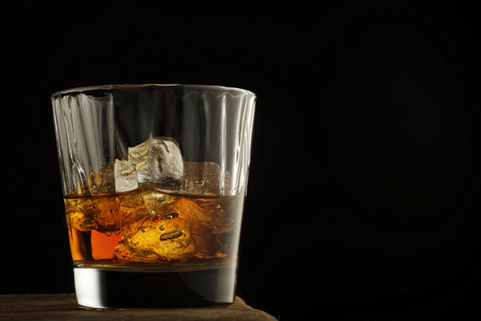 Glass of scotch whiskey and ice on a wooden table.