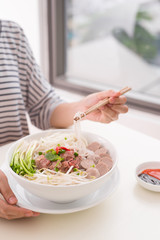 Woman eating traditional Vietnamese Pho noodle using chopsticks.