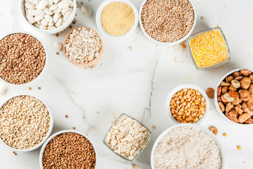 Selection various types cereal grains groats  in different bowl on white marble background, above frame copy space