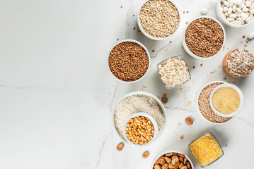 Selection various types cereal grains groats  in different bowl on white marble background, copy space above