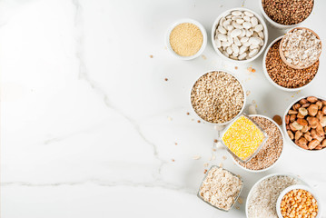 Selection various types cereal grains groats  in different bowl on white marble background, above copy space