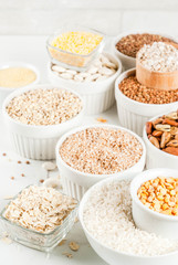 Selection various types cereal grains groats  in different bowl on white marble background,  space for text
