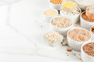 Selection various types cereal grains groats  in different bowl on white marble background,  space for text