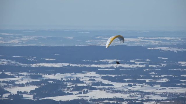 Paraglider circeling over the snow covered landscape of the Allgaeu, Germany, near Fuessen, on the northern edge of the Alps.