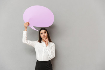 Photo of serious woman in white shirt and black skirt looking upward with thoughtful look and holding copyspace bubble for text, isolated over gray background