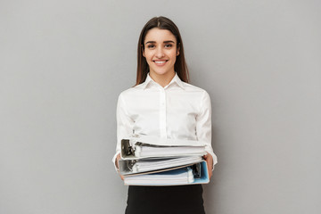 Photo of smiling office woman in white shirt and black skirt holding documents folders in workplace, isolated over gray background
