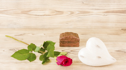 Ein Herz und eine Rose mit einem Geschenk vor einem Holz Hintergrund
