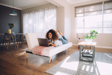 african happy woman lying on couch with laptop