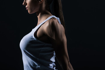 cropped view of female bodybuilder stretching arms, isolated on black