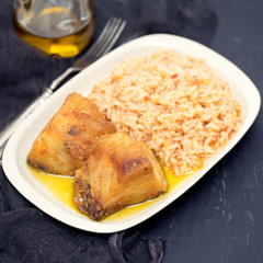 fried cod fish with rice on dish on black ceramic background