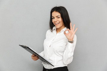 Photo of smiling office woman wearing businesslike outfit holding clipboard with papers and showing...