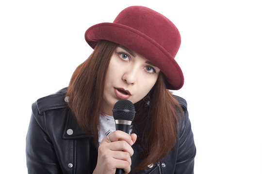 A young woman singing with a microphone wearing a white t-shirt and a red hat in a black leather jacket.