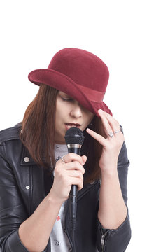 A young woman singing with a microphone wearing a white t-shirt and a red hat in a black leather jacket.