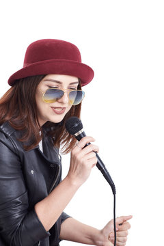 A young woman singing with a microphone wearing a white t-shirt and a red hat in a black leather jacket.