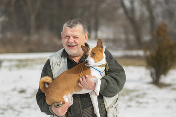 Outdoor portrait of Caucasian senior man taking his lovely basenji dog on the hands. Both are happy chaps.