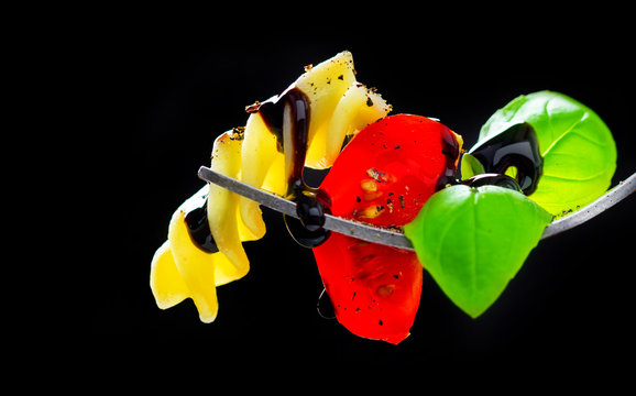 Pasta, tomato and basil on a fork, isolated against a black background