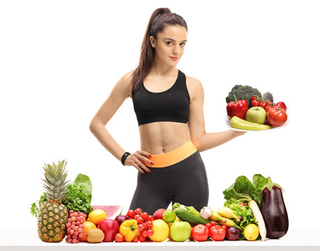 Fitness girl behind a table with fruit and vegetables holding a plate
