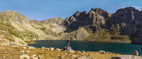 Górskie jezioro w Tatrach. Kobieta stojąca nad brzegiem jeziora. Turystyka górska. - obrazy, fototapety, plakaty