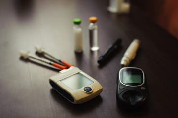 medicine, diabetes and health care concept - close up of blood sugar test stripe, glucometer, insulin pen and other diabetic tools on table
