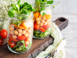 Fresh salad lunch with chickpeas, tomatoes, carrots and valerian served in mason jars