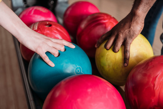 cropped shot of man and woman taking bowling balls from stand