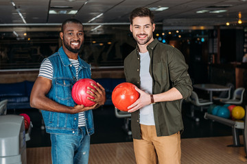 happy young men with balls at bowling club looking at camera