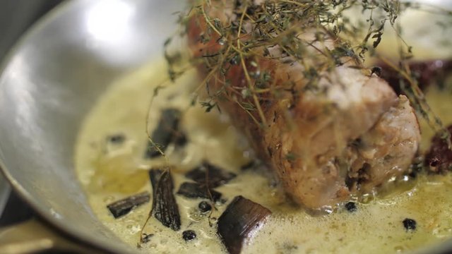 Fresh meatloaf or piece of meat fried in frying pan in herbs and spices. Bubbles of boiling oil in hot metal pan. High Angle. Preparation of fatty and unhelpful food in restaurant, cafe or catering.