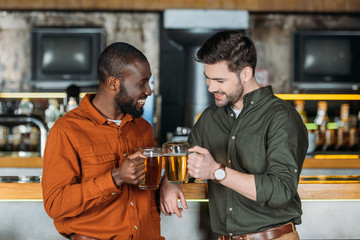 handsome young men with mugs of beer clinking at bar counter