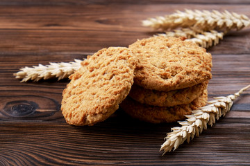 Healthy vegan integral cookies made of hazelnut powder on dark brown wooden table background. Home made vegetarian sugarless & gluten free snack with nuts. Decorative wheat spica. Close up, copy space