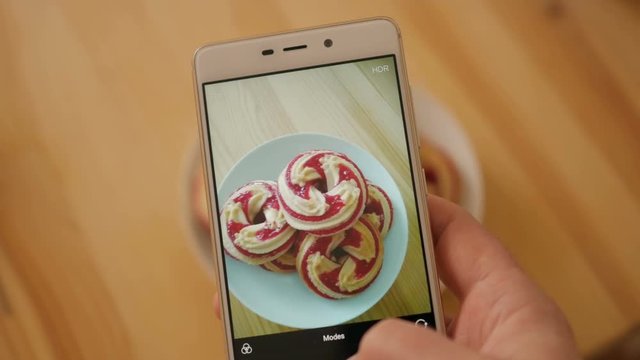 Closeup of man hand making photo of sweet dessert on mobile phone.  Male photographs on the smartphone a round soft biscuit on a wooden table close up.