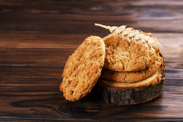 Healthy vegan integral cookies made of hazelnut powder on wooden slice coaster, wood table background. Home made vegetarian, gluten free snack with nuts. Decorative wheat spica. Close up, copy space.