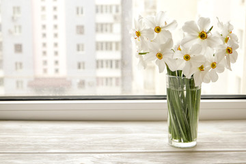 White yellow daffodil, daffadowndilly, narcissus, jonquil flowers in glass vase on wooden windowsill, no window wiev. Happy mother's day greeting card. Close up, copy space, still life, background.