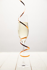 Closeup view of champagne glass wrapped by serpentine on white wooden table, holiday concept