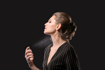 Beautiful young woman with bottle of perfume on black background