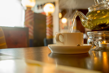 transparent teapot with green hot tea and a cup on a wooden table