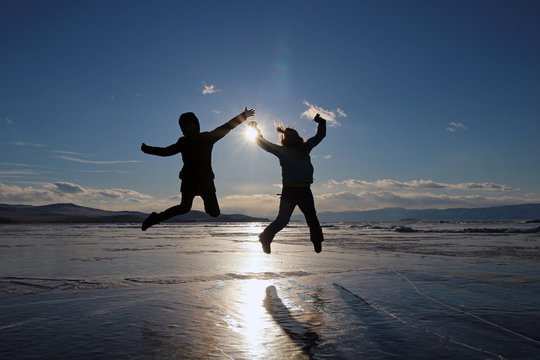 Silhouettes of happy young people jumping over the ice of lake Baikal at sunset.