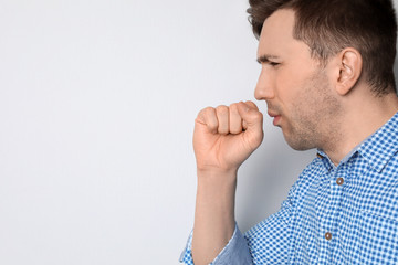 Young man coughing on light background