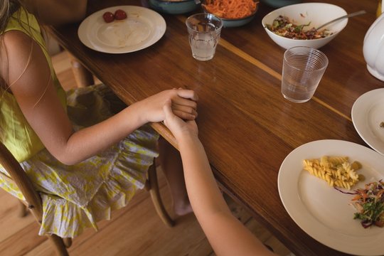 Sibling praying together before having lunch in kitchen at home