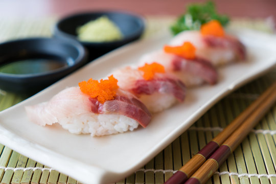 Hamachi sushi on white plate along with Japanese sauce and green leaf decoration, Japanese food, close up at sushi ..